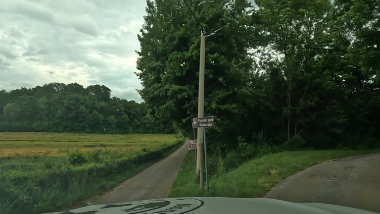 Smalle landweg met wegwijzer naar Pećinski Park Grabovača, omringd door velden en bos in Kroatië.