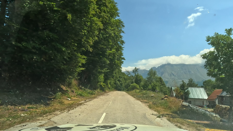 Slechte asfaltweg met bomen en boerderijtje langs de route naar Spomenik Sutjeska