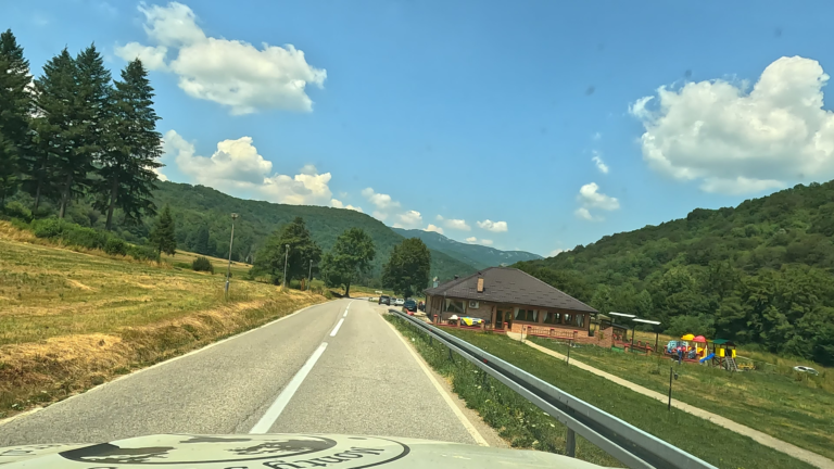 Asfaltweg met restaurant en bergen tegenover Spomenik Sutjeska monument