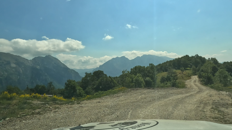 Gravelpad met uitzicht op loofbomen en rotsachtige berghellingen langs de route naar Spomenik Sutjeska