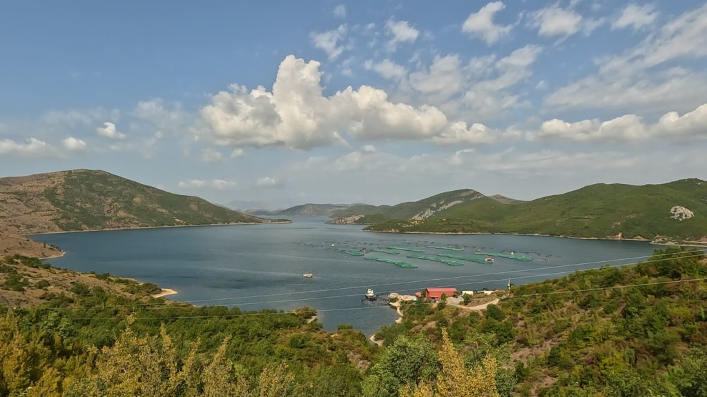 Uitzicht vanaf Komani Lake viewpoint over het meer met Kilic Fish Farm en groene bergen.