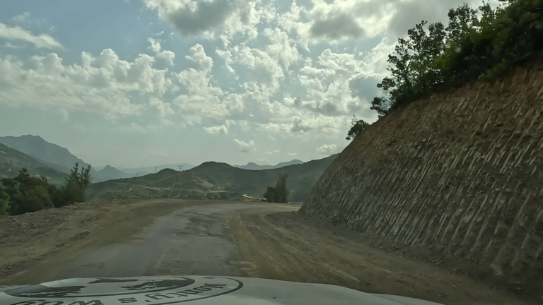 Kronkelende SH25 met losse gravel en steile bergwand langs de weg.