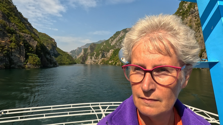 Selfie op het passagiersdek met Komani Lake en bergen op de achtergrond.
