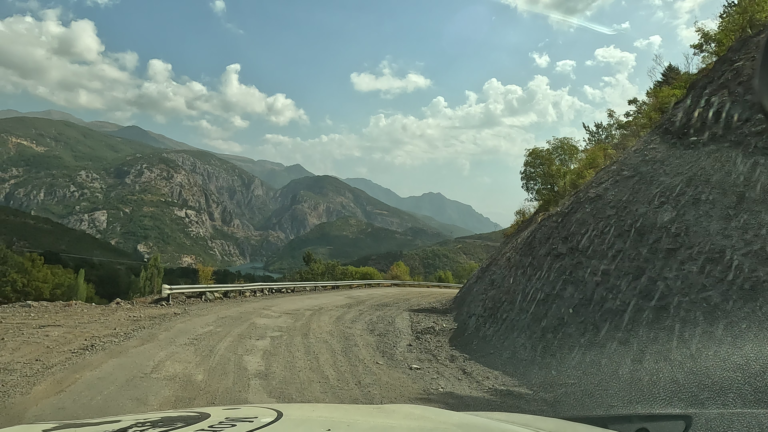 Kronkelende bergweg met Komani Lake zichtbaar aan de zijkant.