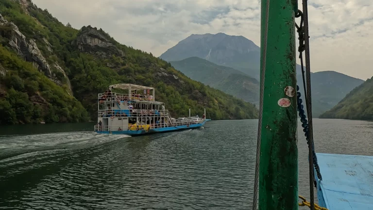Tegemoetkomende ferry op Komani Lake met bergen op de achtergrond.