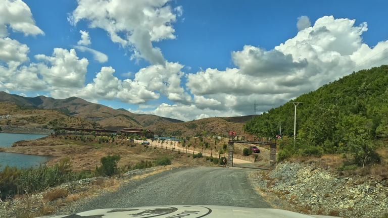 Eerste zicht op het Qafë Mollë-stuwmeer in Albanië met een gravelweg en ingang naar Real Park Mirdit.