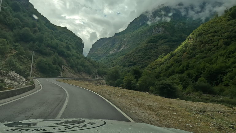 Bochtige bergweg met aan beide kanten bergen en laaghangende grijze wolken boven de toppen.