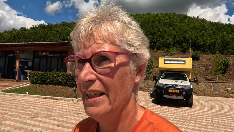 Selfie bij camper, Monty, op de parkeerplaats van real park Mirdit naast het toiletgebouw in bergachtig Albanië. Beschrijving 1: