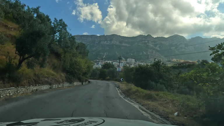 Uitzicht vanaf bergweg SH 38 op Krujë in de vallei met bergen op de achtergrond.