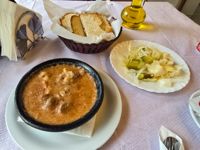 Lunch bestaand uit een stoofgerecht met rundvlees geserveerd met brood en ingelegde kool en augurk geserveerd op wit servies.
