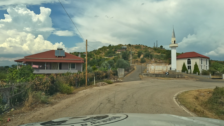 Huis langs SH3 (Albanië) vlak voor een bocht met witte moskee en heuvel met verspreide huizen