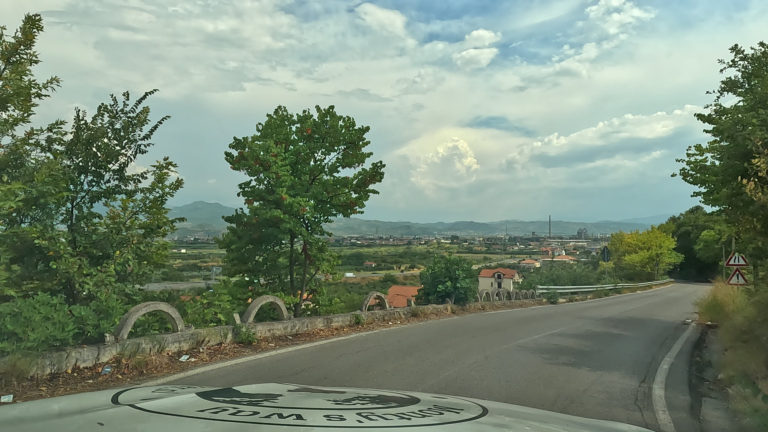 Betonnen vangrails met bogen langs SH3 (Albanië) met uitzicht op vallei met grasland en huizen en bergen