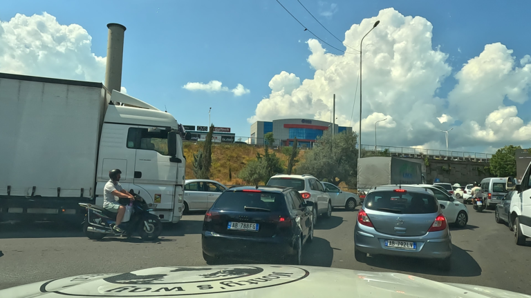 Auto’s staan in lange rijen rond een drukke rotonde in Tirana met langzaam verkeer.
