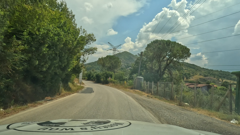De SH3 loopt vanuit Tirana langs ene weg met bomen links en een boerderij op lager gelegen terrein aan de rechterkant.