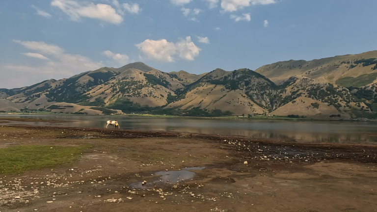Een panoramisch beeld van Lago Matese met een drinkend paard op het grasland en de bergen rondom het meer.