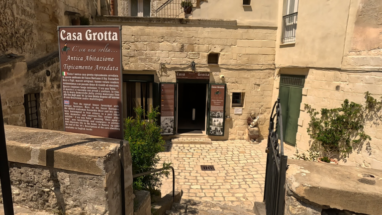 Tijdens mijn bezoek aan Matera kijk ik door het smeedijzeren hek naar de ingang van Casa Grotta di Vico Solitario