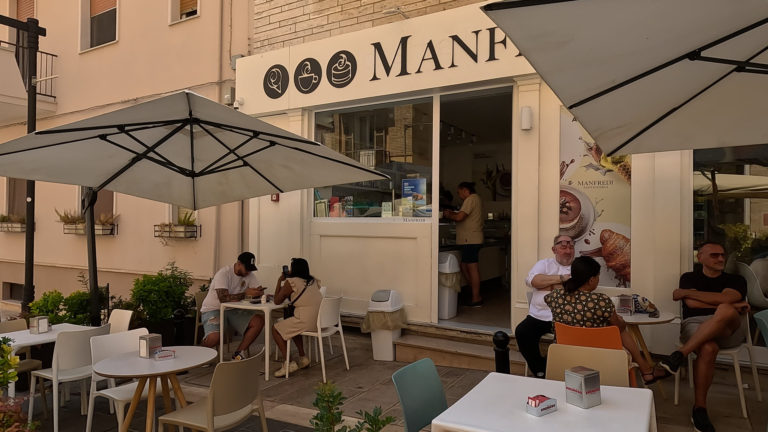 Ik kijk vanaf de straat naar Gelateria Manfredo waar parasols voor de zaak staan